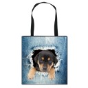 Bolsa shopper para mujer con estampado realista de un animal asomando de la tela de mezclilla rasgada. Lona y poliéster. Asas negras. Forma 11