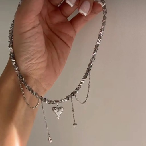 Šedý náhrdelník z drobných hranatých korálků s vrstvenými řetízky, srdíčkem a visícími detaily, asymetrický dekorativní šperk