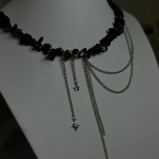 Zwarte ketting van onregelmatige steentjes met hangende kettingen, een ster en een klein kruisje, opvallende asymmetrische decoratieve sieraden